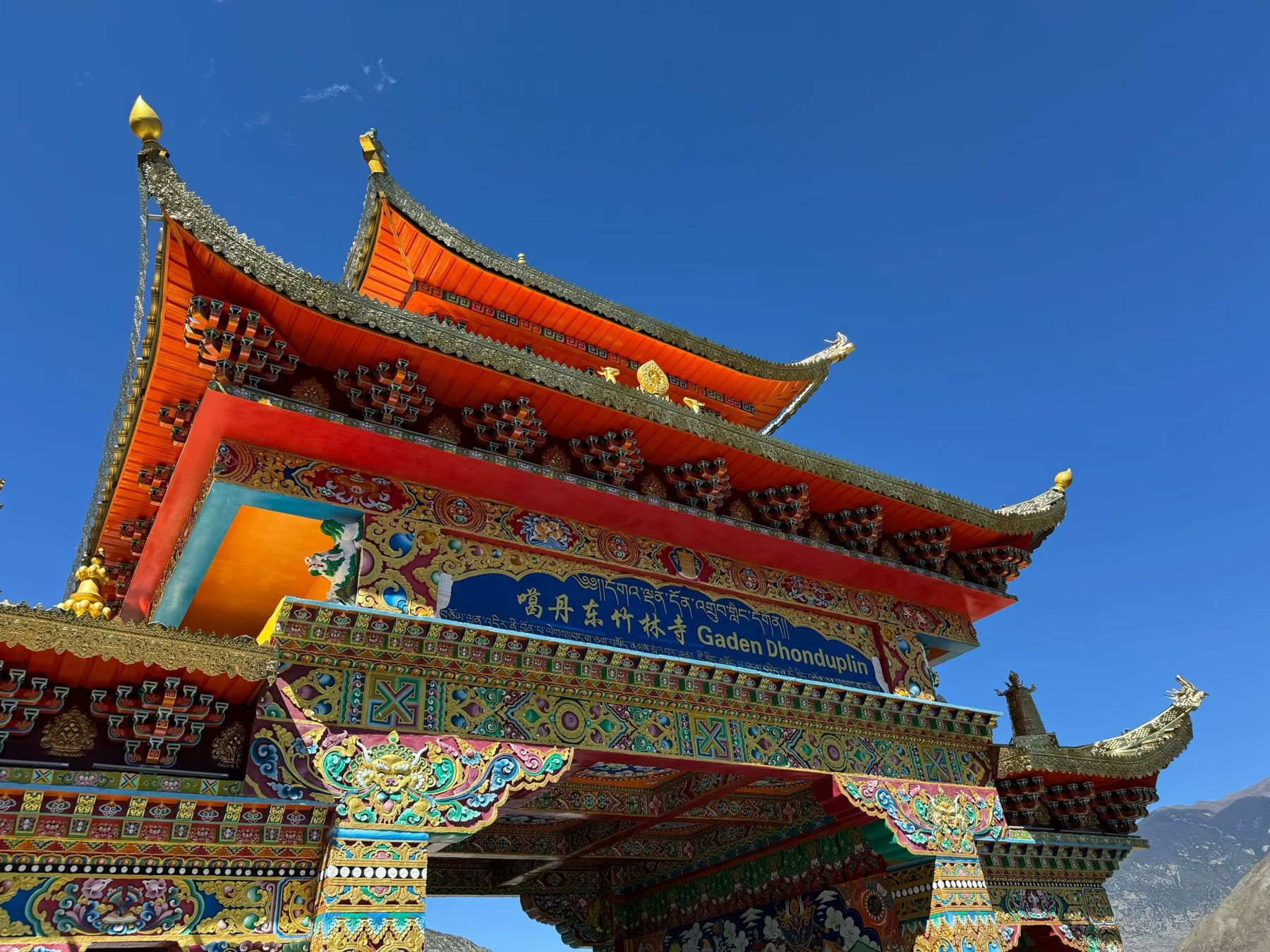 The richly painted red and gold gate of a Tibetan monastery under a deep blue sky