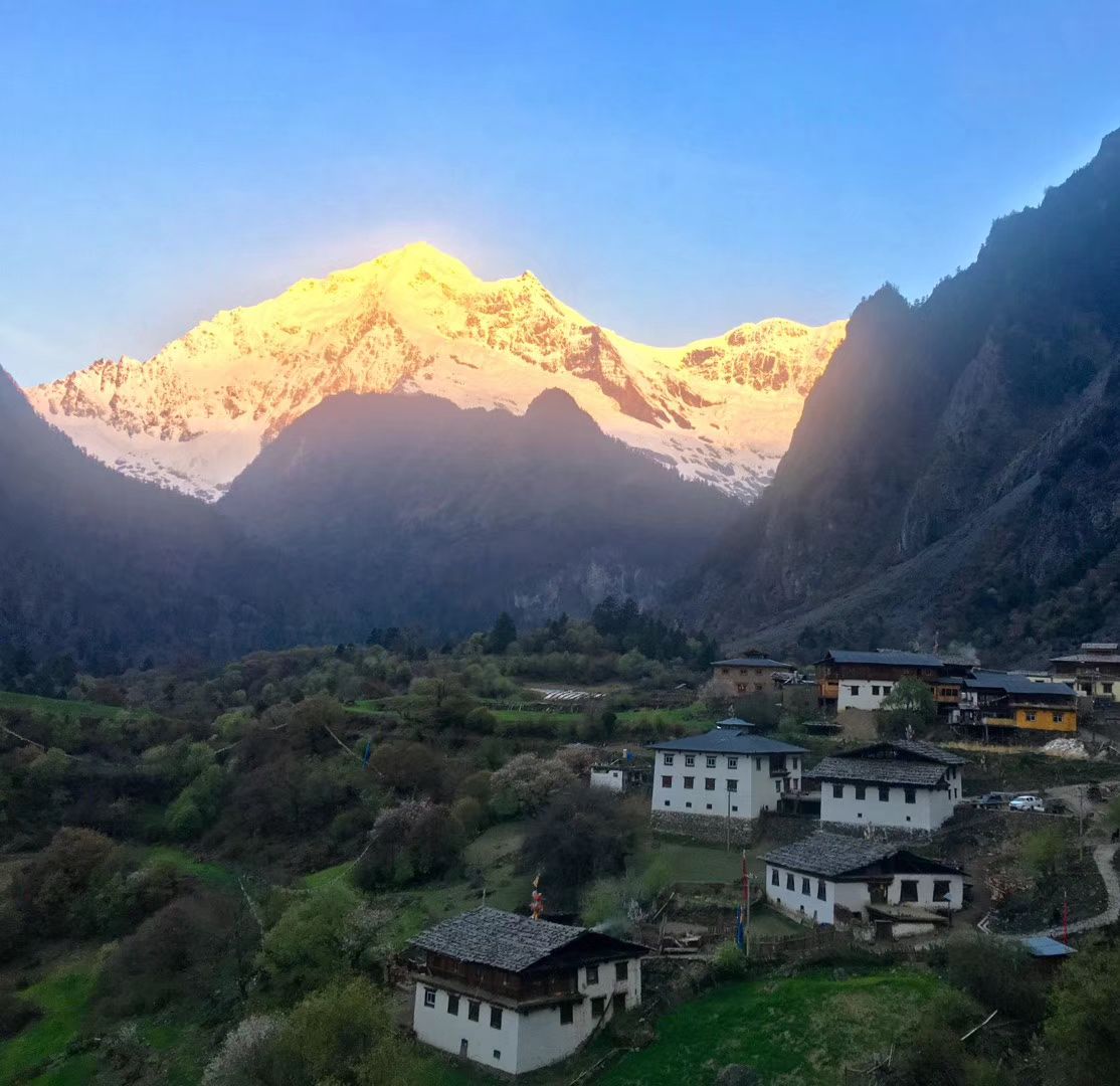 Snow peaks glowing gold at sunrise above the houses of Upper Yubeng