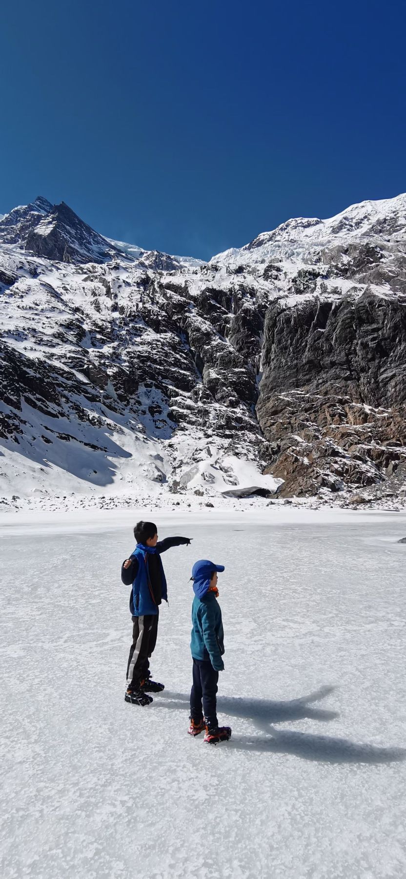 Two children on a frozen lake in front of snow-covered peaks