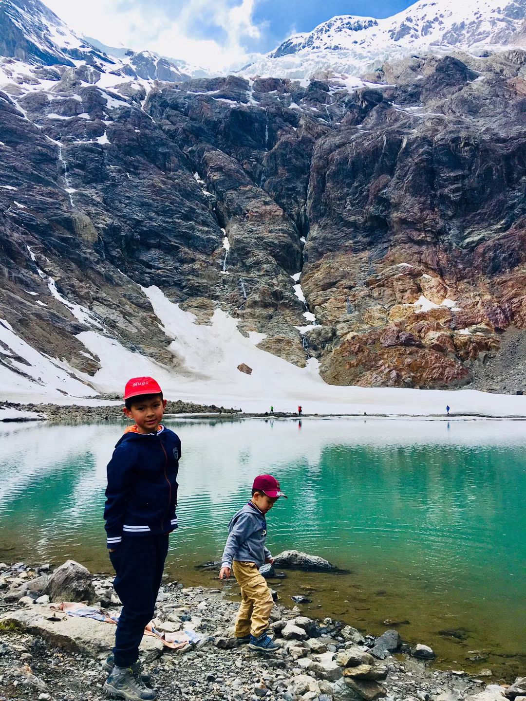 Two boys beside a turquoise lake below a snowy cirque