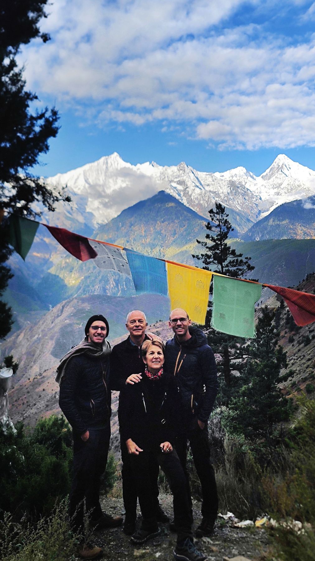 Four people in front of prayer flags with the Kawa Karpo range behind them