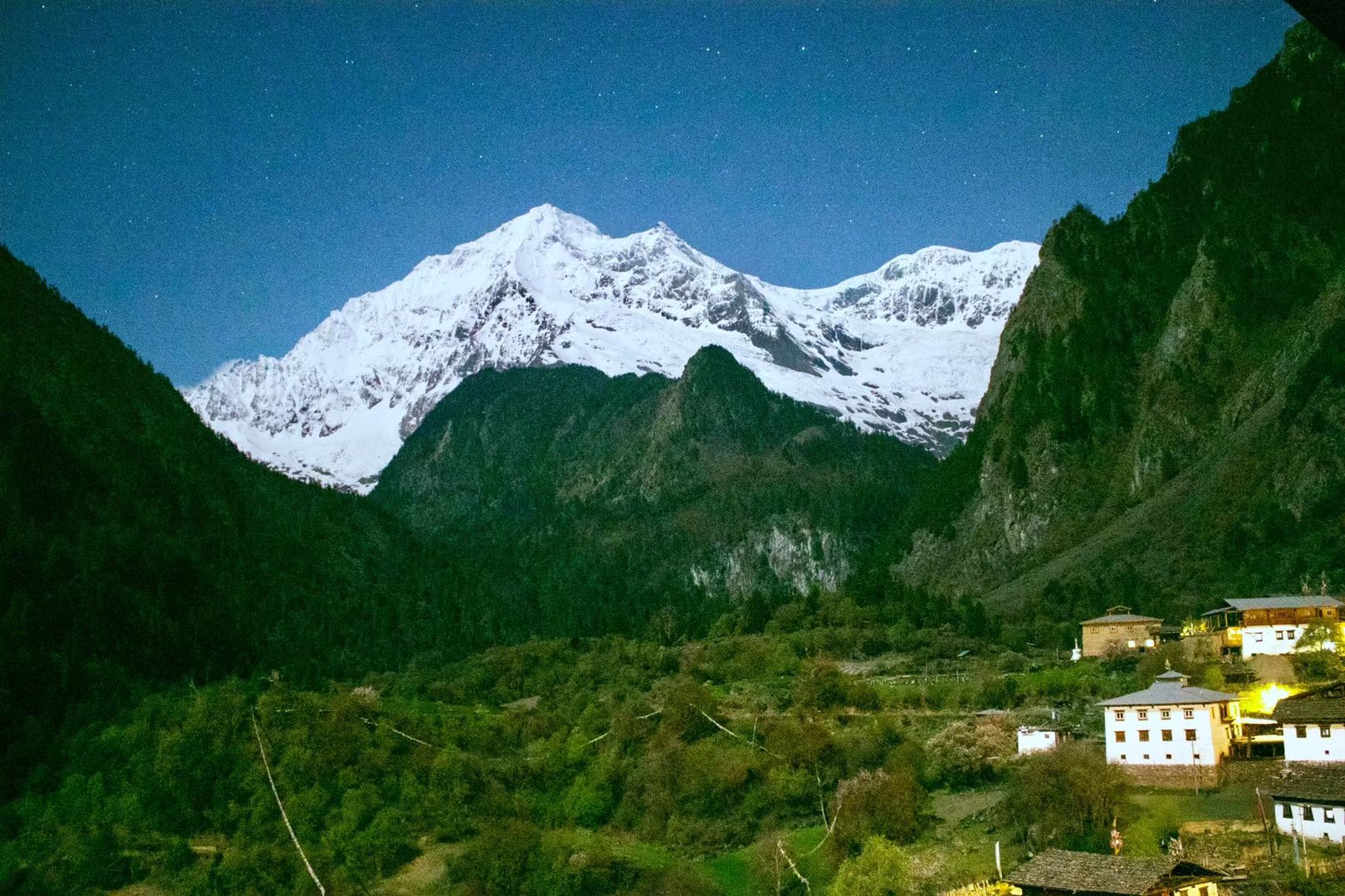 A snow peak under a starry night sky above the houses of Yubeng