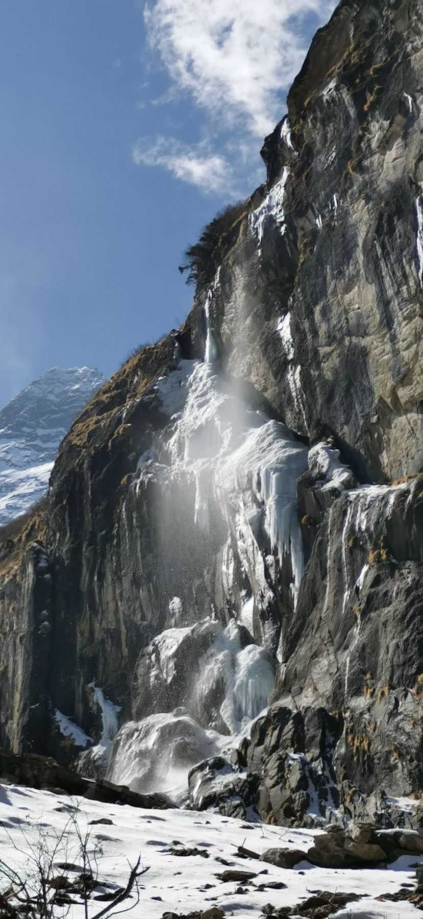 A frozen waterfall on a rock face with snow at its foot