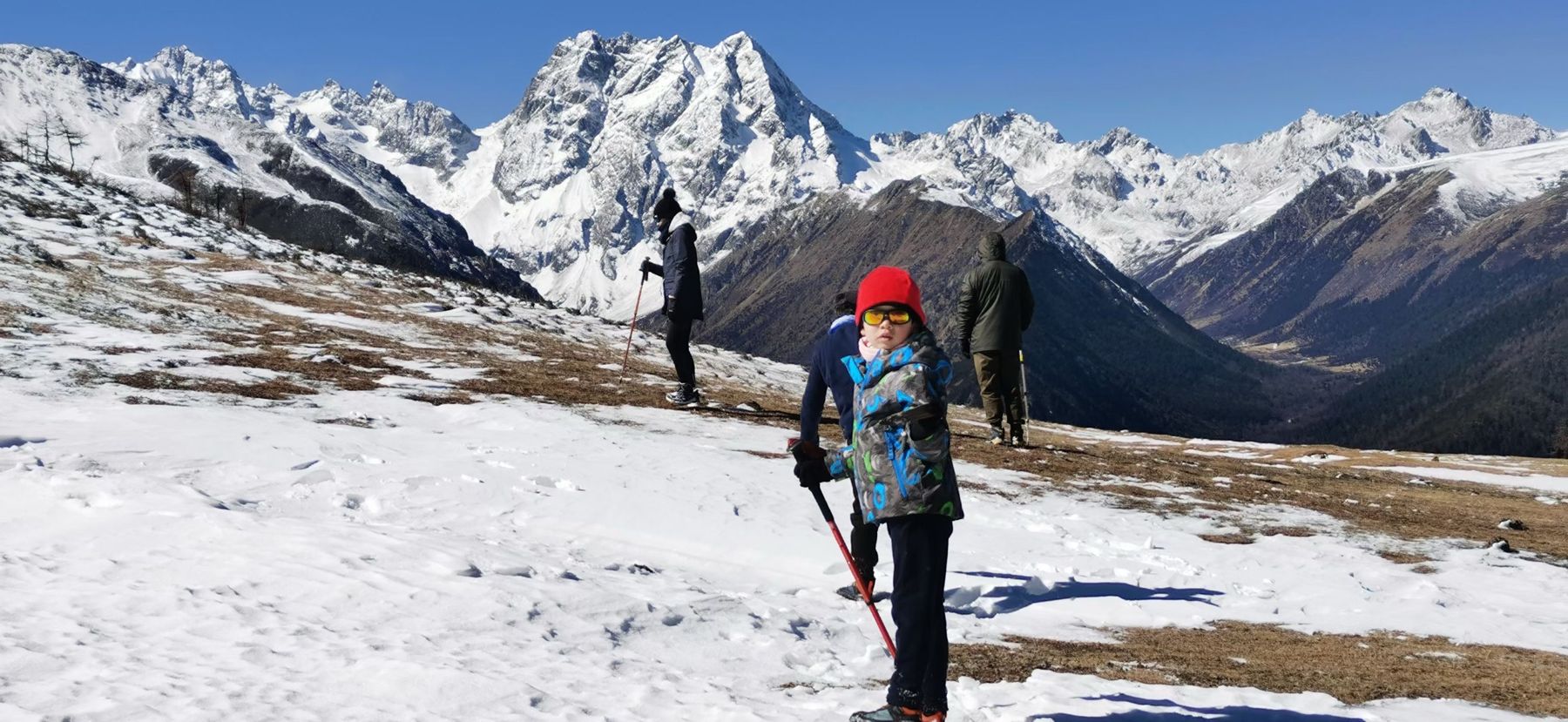 A child in a red hat on a snowy slope with a snow-covered range behind