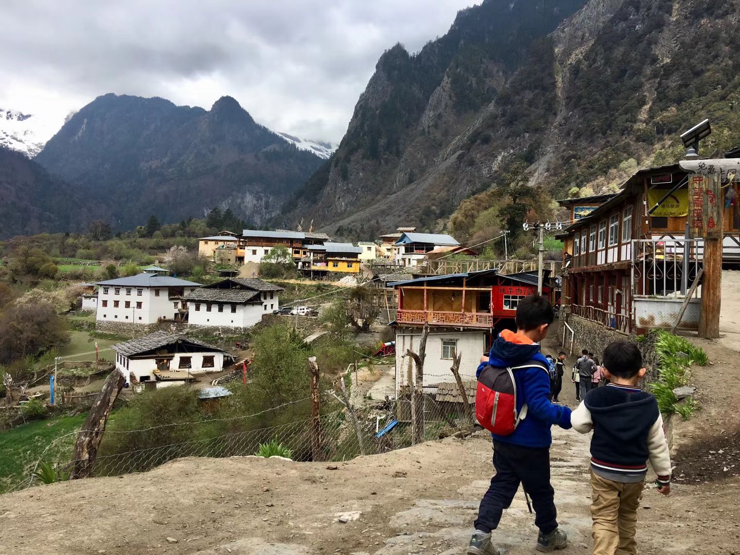 Two children walking toward the timber houses of Upper Yubeng under a mountain