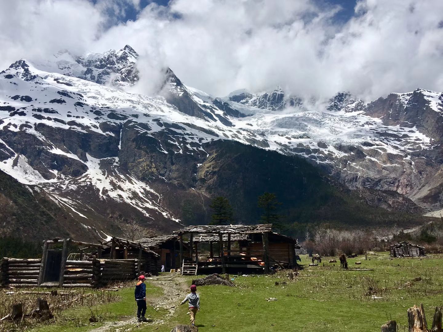 Wooden huts in a green pasture below glaciated peaks