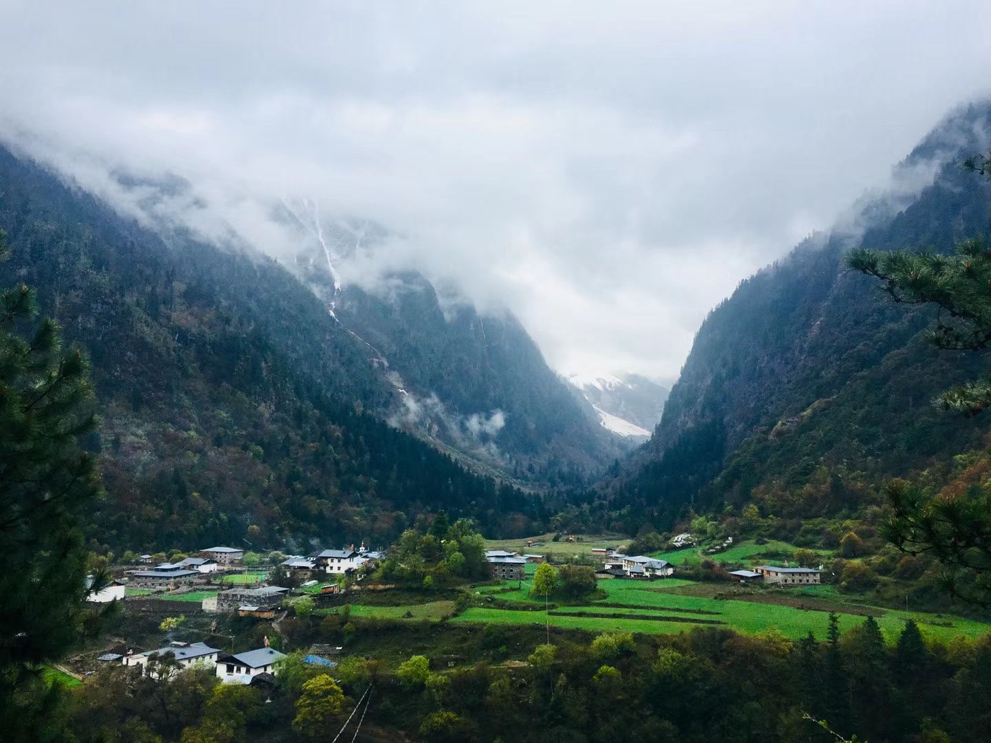 A village among green fields in a valley under low cloud